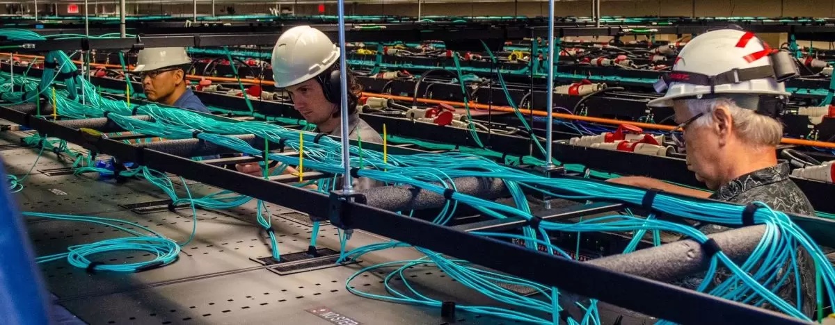 L-R: Junseong Heo, Dave Cooper, David Carver TACC employees work on the network cabling above the racks of Frontera. TACC systems have always been built and maintained in-house by their dedicated staff.
Credit: TACC
